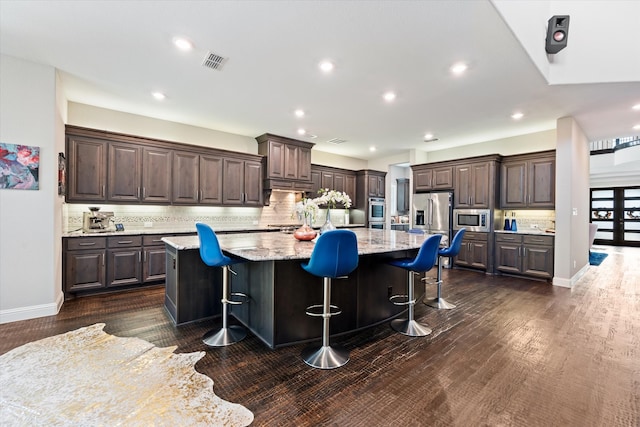 kitchen featuring a large island, backsplash, dark brown cabinets, and a breakfast bar