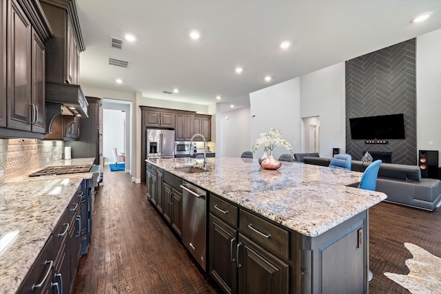 kitchen with light stone countertops, appliances with stainless steel finishes, an island with sink, and dark brown cabinetry