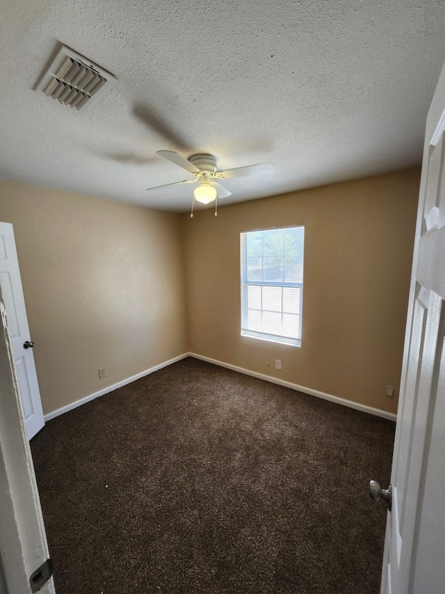 spare room with a textured ceiling, ceiling fan, and dark colored carpet