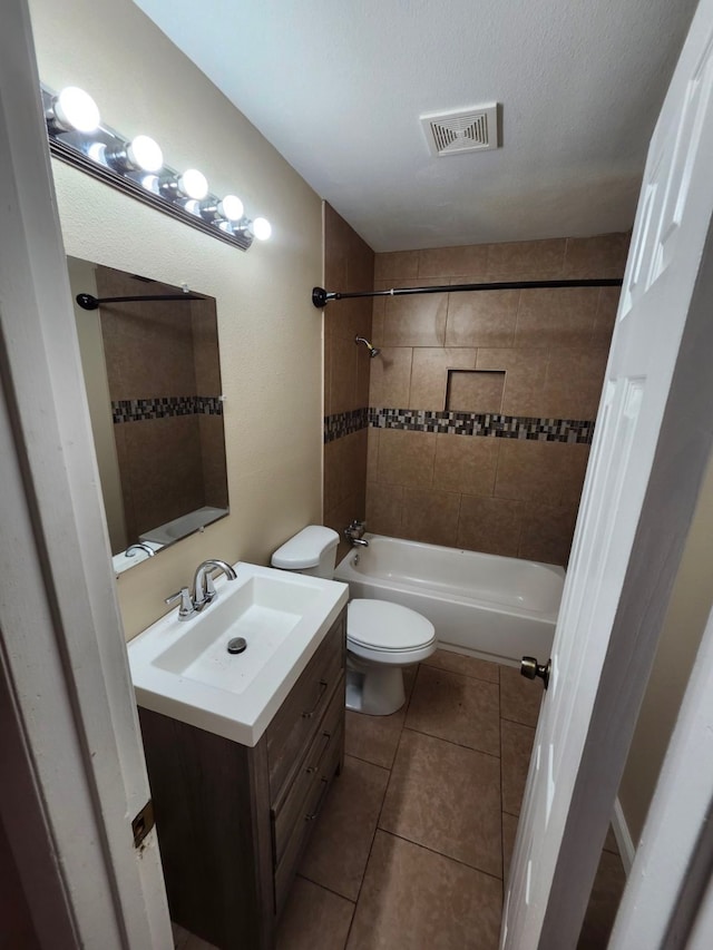 full bathroom featuring a textured ceiling, toilet, vanity, tiled shower / bath combo, and tile patterned flooring