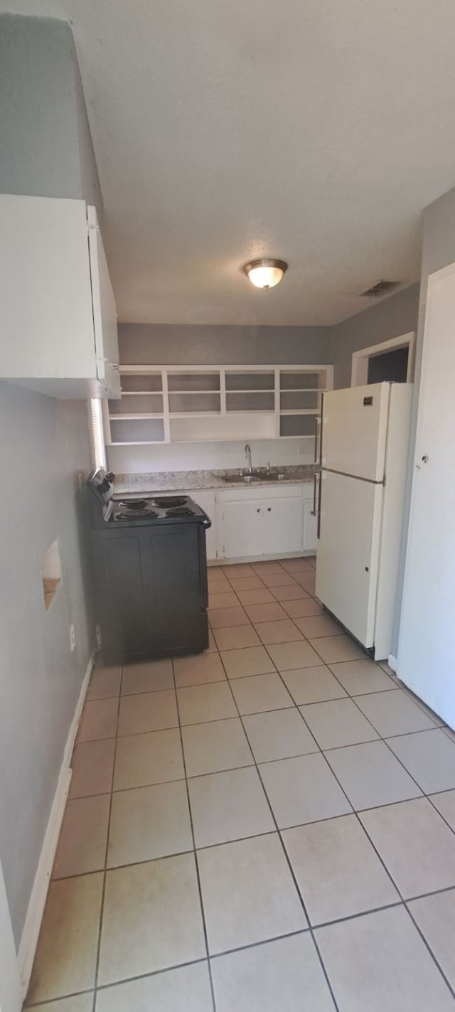 kitchen featuring sink, light tile patterned flooring, white refrigerator, black range with electric stovetop, and white cabinets