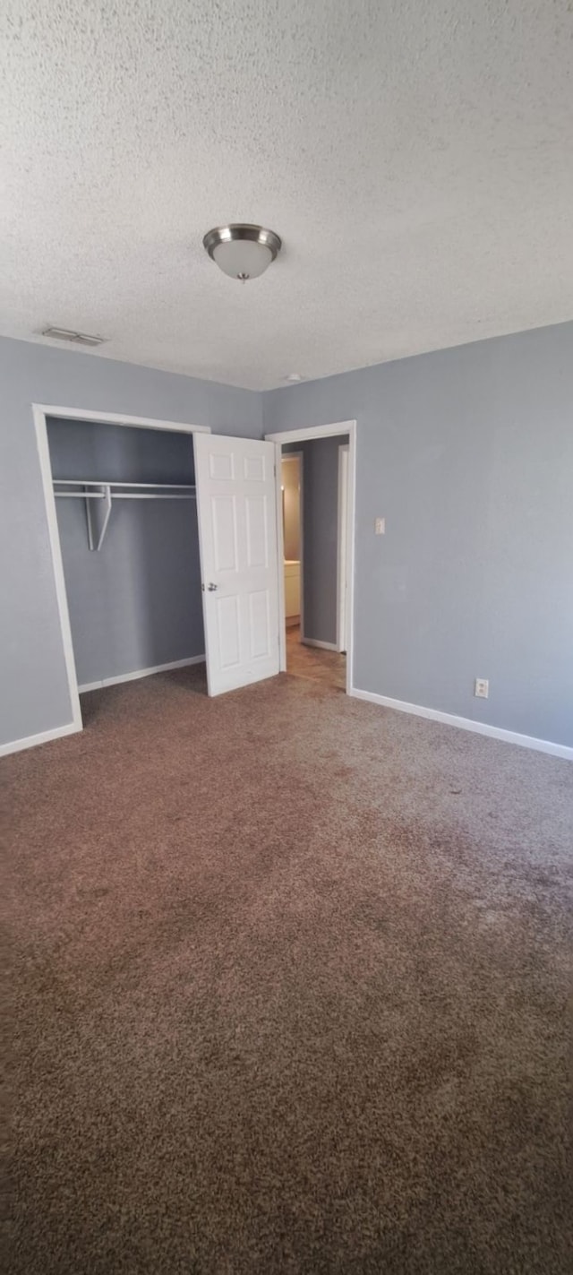 unfurnished bedroom featuring dark carpet, a textured ceiling, and a closet