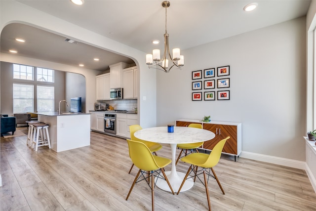 dining area with light hardwood / wood-style floors, sink, and an inviting chandelier