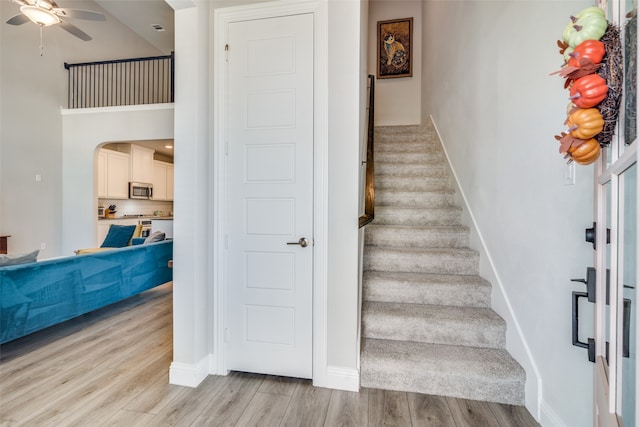 stairway with a towering ceiling, hardwood / wood-style flooring, and ceiling fan