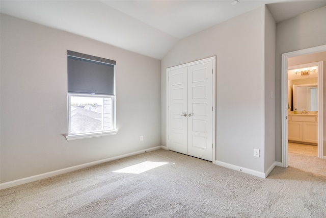 unfurnished bedroom with lofted ceiling, a closet, light colored carpet, and ensuite bathroom