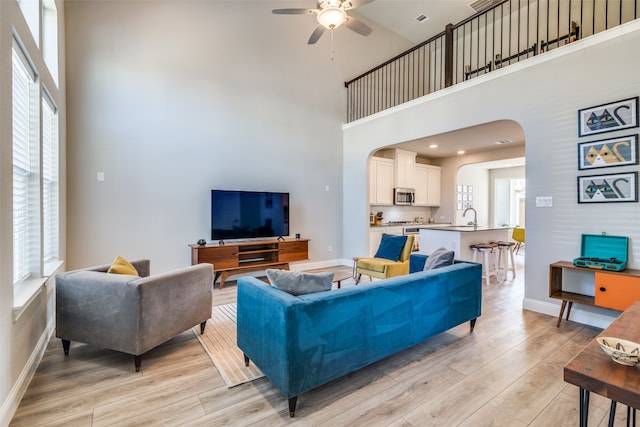 living room featuring a healthy amount of sunlight, sink, light hardwood / wood-style flooring, and a towering ceiling