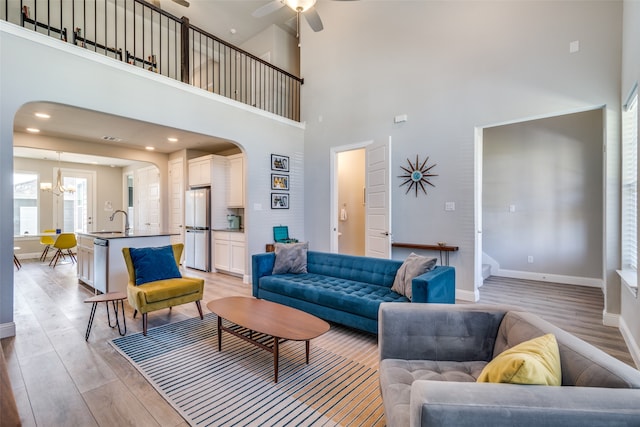 living room with sink, a towering ceiling, light hardwood / wood-style flooring, and ceiling fan with notable chandelier