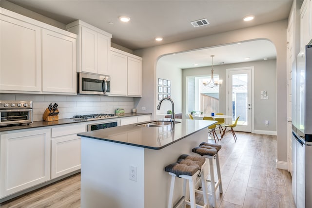 kitchen with a center island with sink, sink, pendant lighting, light wood-type flooring, and appliances with stainless steel finishes