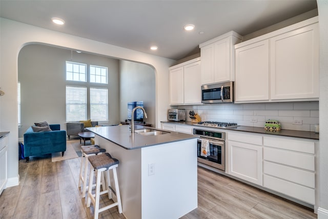 kitchen with appliances with stainless steel finishes, sink, light hardwood / wood-style floors, and an island with sink