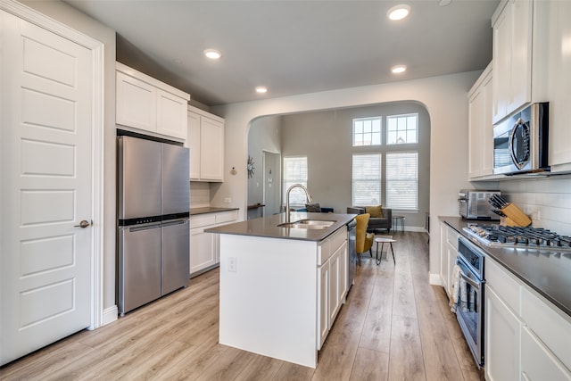 kitchen featuring light hardwood / wood-style flooring, an island with sink, sink, white cabinets, and appliances with stainless steel finishes