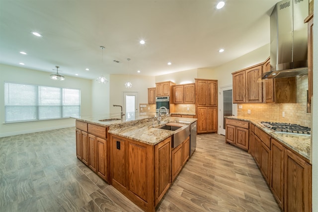 kitchen with appliances with stainless steel finishes, sink, a large island, light hardwood / wood-style floors, and wall chimney exhaust hood