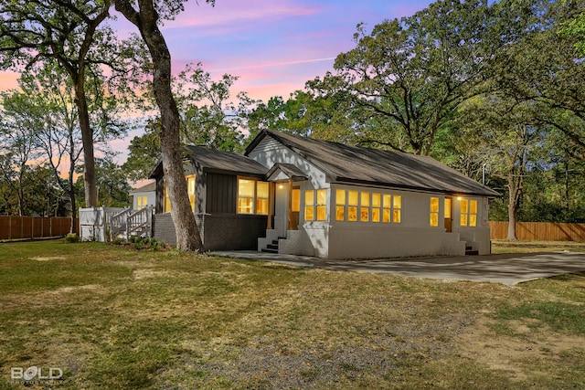 back house at dusk featuring a patio and a lawn