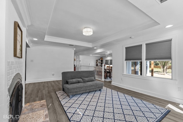 living area featuring dark wood-style floors, a tray ceiling, a fireplace, and crown molding