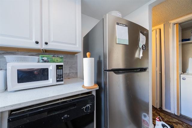 kitchen with washer / clothes dryer, backsplash, white cabinetry, light stone counters, and stainless steel refrigerator