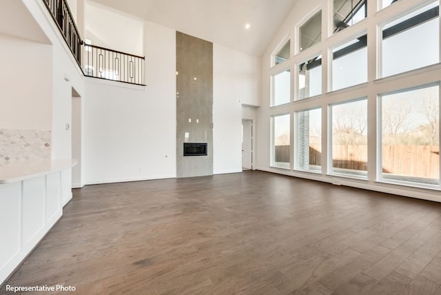 unfurnished living room with dark wood-type flooring, a large fireplace, heating unit, and a high ceiling