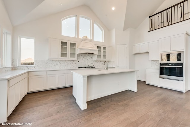 kitchen featuring white cabinetry, oven, a center island with sink, and light hardwood / wood-style flooring