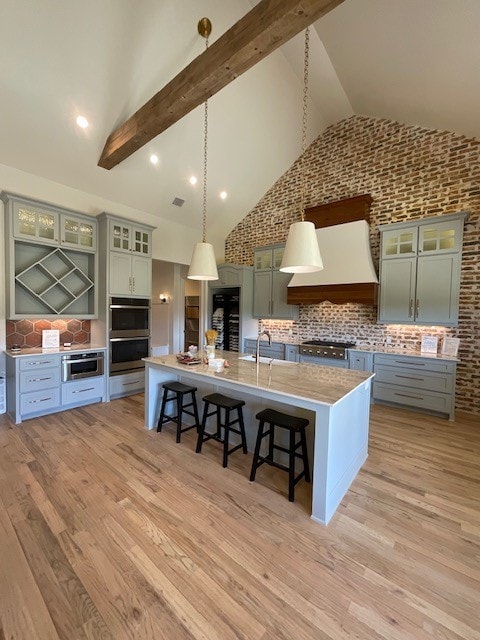 kitchen featuring hanging light fixtures, a center island with sink, a breakfast bar, premium range hood, and high vaulted ceiling