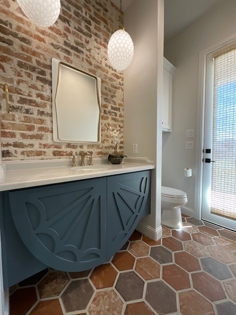 bathroom featuring vanity, toilet, and brick wall