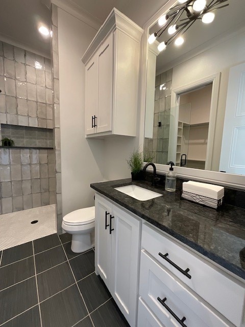 bathroom featuring a tile shower, an inviting chandelier, toilet, vanity, and tile patterned floors