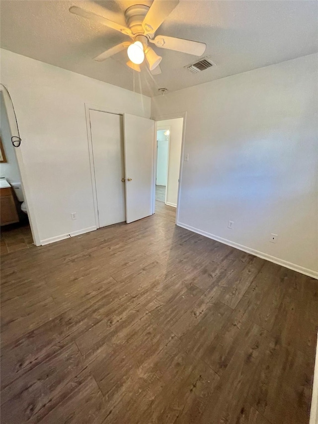 unfurnished bedroom featuring ensuite bath, ceiling fan, dark wood-type flooring, a textured ceiling, and a closet