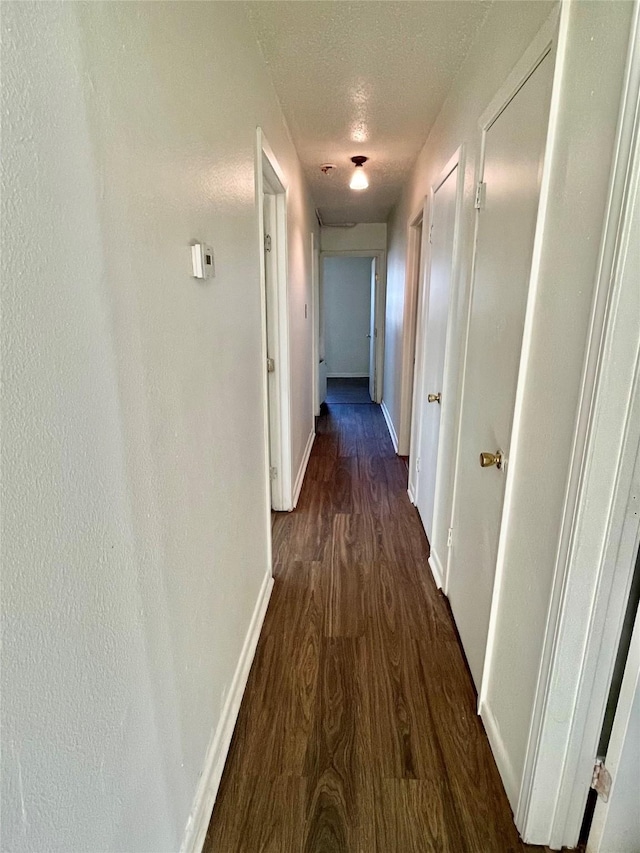 hallway with a textured ceiling and dark hardwood / wood-style floors