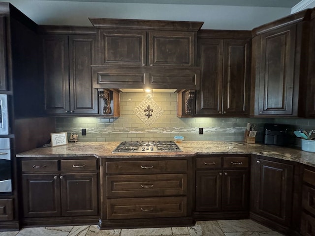 kitchen featuring appliances with stainless steel finishes, dark brown cabinetry, light stone counters, and backsplash