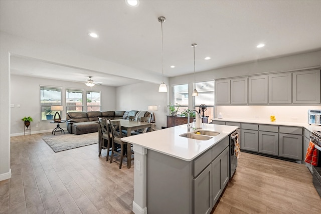 kitchen with appliances with stainless steel finishes, sink, gray cabinets, light hardwood / wood-style flooring, and a kitchen island with sink