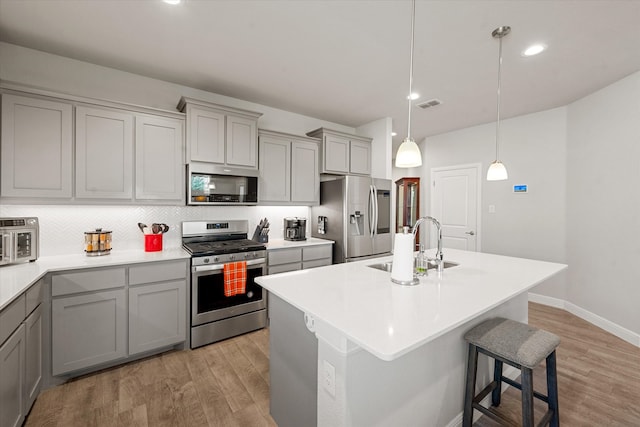 kitchen featuring hanging light fixtures, a center island with sink, appliances with stainless steel finishes, light hardwood / wood-style flooring, and sink