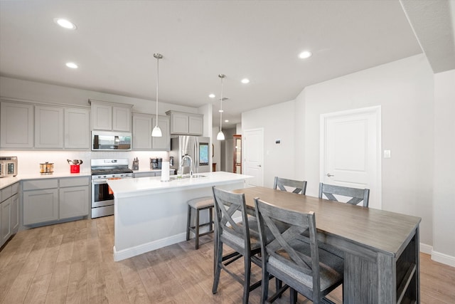 kitchen featuring an island with sink, decorative light fixtures, light wood-type flooring, gray cabinets, and appliances with stainless steel finishes