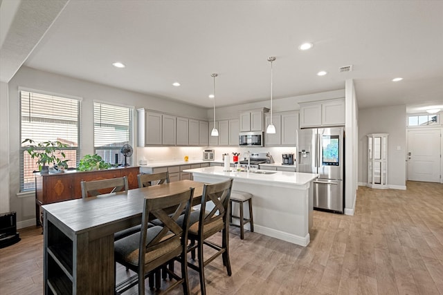 kitchen featuring a kitchen island with sink, a kitchen breakfast bar, hanging light fixtures, appliances with stainless steel finishes, and light hardwood / wood-style floors