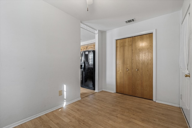 unfurnished bedroom with a closet, light hardwood / wood-style flooring, black refrigerator with ice dispenser, and ceiling fan