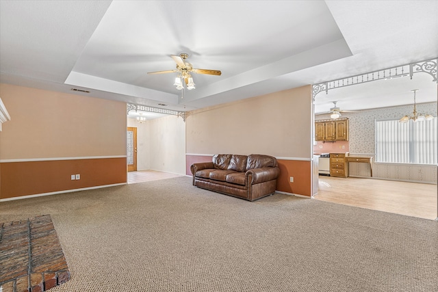 carpeted living room featuring a raised ceiling and ceiling fan with notable chandelier