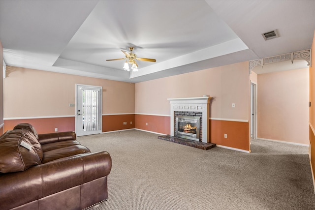 living room featuring ceiling fan, carpet, a tray ceiling, and a fireplace