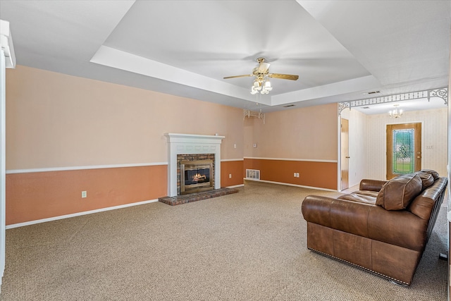 living room with carpet floors, a tray ceiling, a fireplace, and ceiling fan