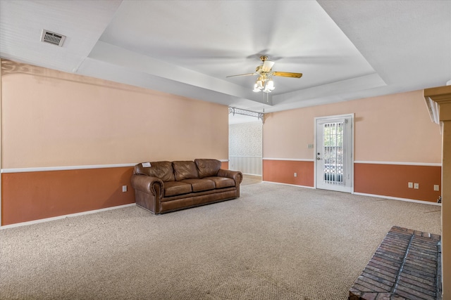 living area with ceiling fan, a tray ceiling, and carpet floors