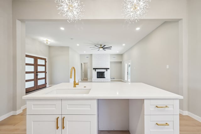 kitchen with light hardwood / wood-style flooring, white cabinets, a kitchen island with sink, and sink