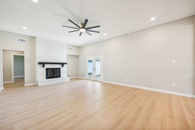 unfurnished living room featuring light hardwood / wood-style flooring, french doors, a fireplace, and ceiling fan