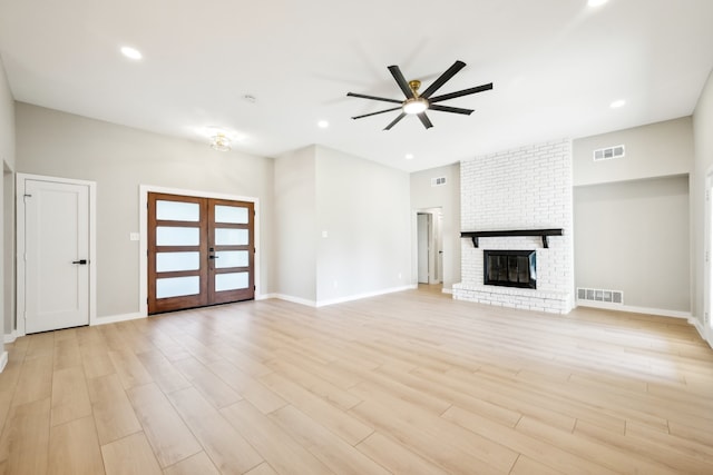 unfurnished living room featuring light hardwood / wood-style floors, french doors, ceiling fan, and a brick fireplace