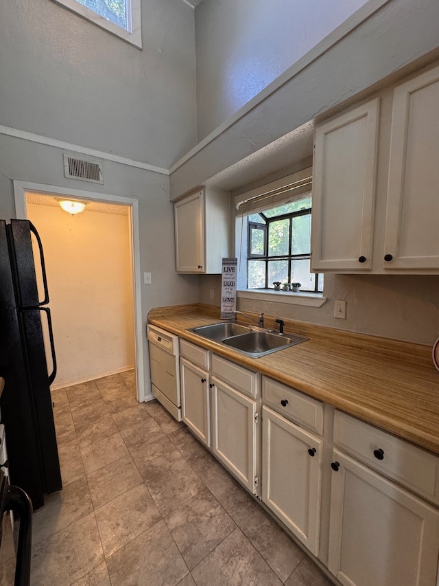 kitchen with sink, white dishwasher, white cabinetry, vaulted ceiling, and black refrigerator