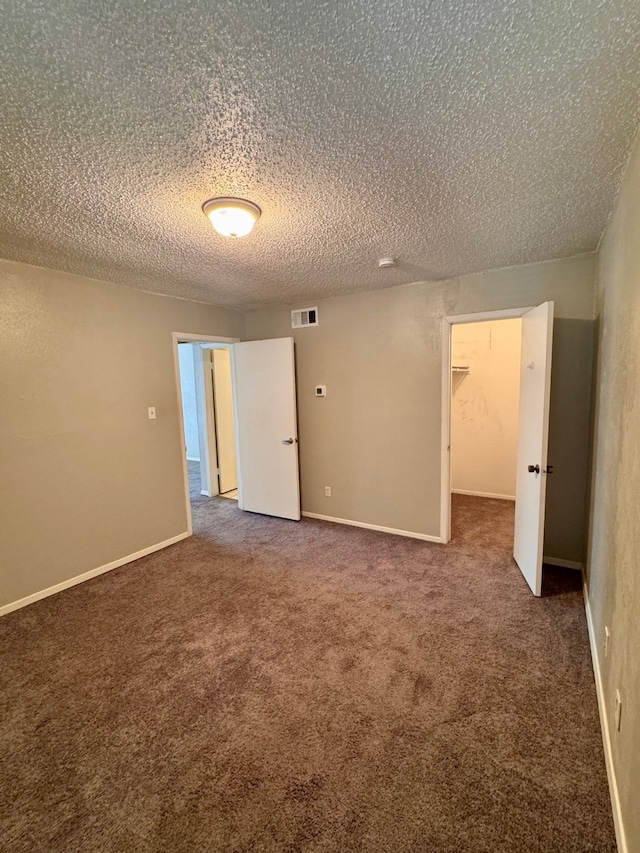 unfurnished room featuring a textured ceiling and dark colored carpet