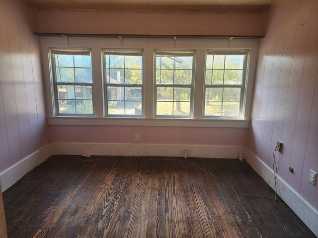 empty room with dark wood-type flooring, a healthy amount of sunlight, and wooden walls