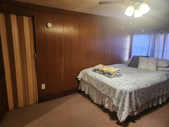 carpeted bedroom featuring ceiling fan and wood walls