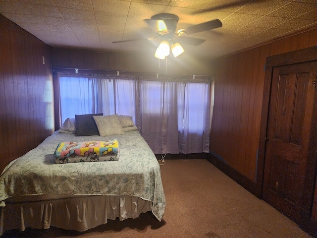 carpeted bedroom featuring ceiling fan and wood walls