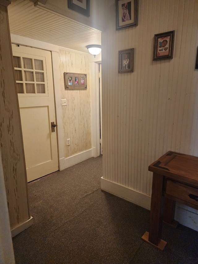 hall featuring dark carpet and wood walls