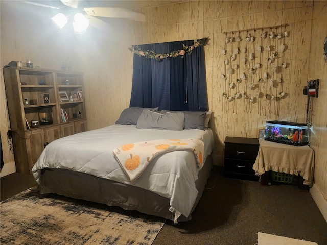 bedroom with ceiling fan, wood walls, and dark carpet