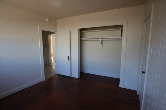 unfurnished bedroom featuring a closet, dark hardwood / wood-style floors, a textured ceiling, and wooden walls