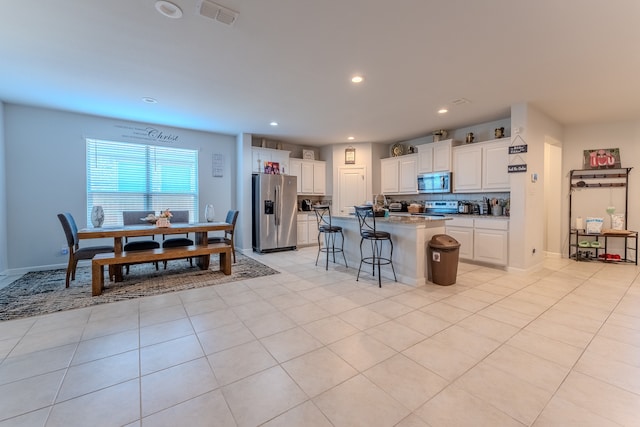 kitchen with appliances with stainless steel finishes, a kitchen breakfast bar, a kitchen island with sink, light tile patterned floors, and white cabinets