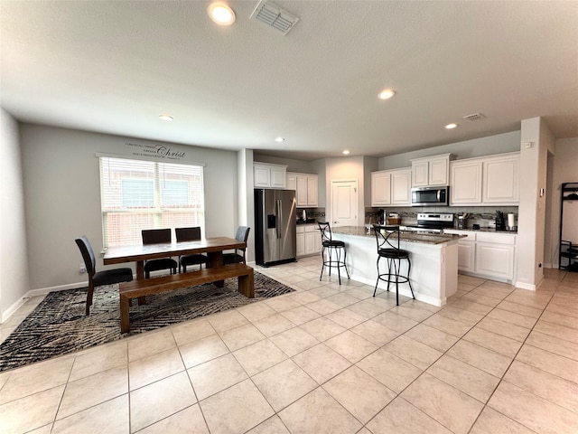 kitchen featuring a kitchen bar, appliances with stainless steel finishes, decorative backsplash, white cabinets, and an island with sink