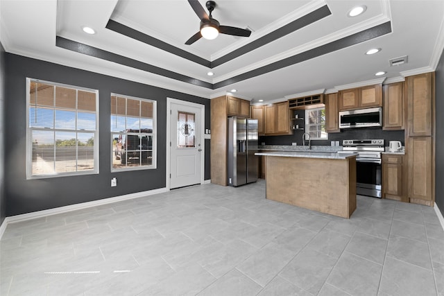 kitchen featuring appliances with stainless steel finishes, a raised ceiling, a center island, ceiling fan, and crown molding