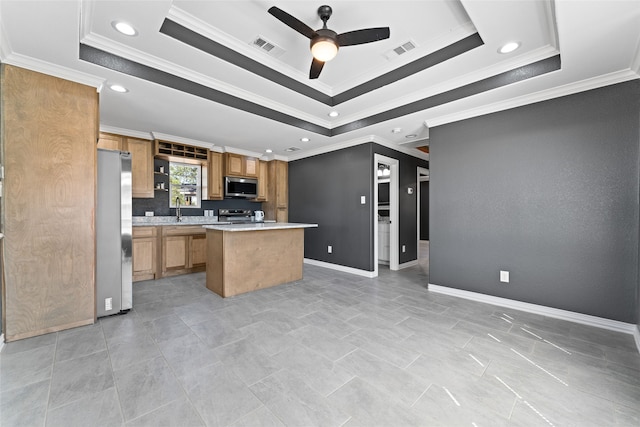 kitchen featuring appliances with stainless steel finishes, crown molding, a center island, and a tray ceiling